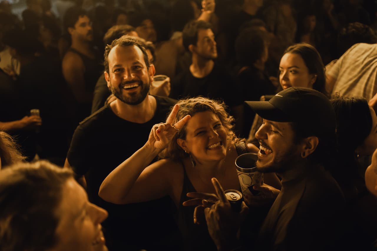 Grupo de amigos ri e conversa colado no meio da multidão iluminada por luz âmbar
