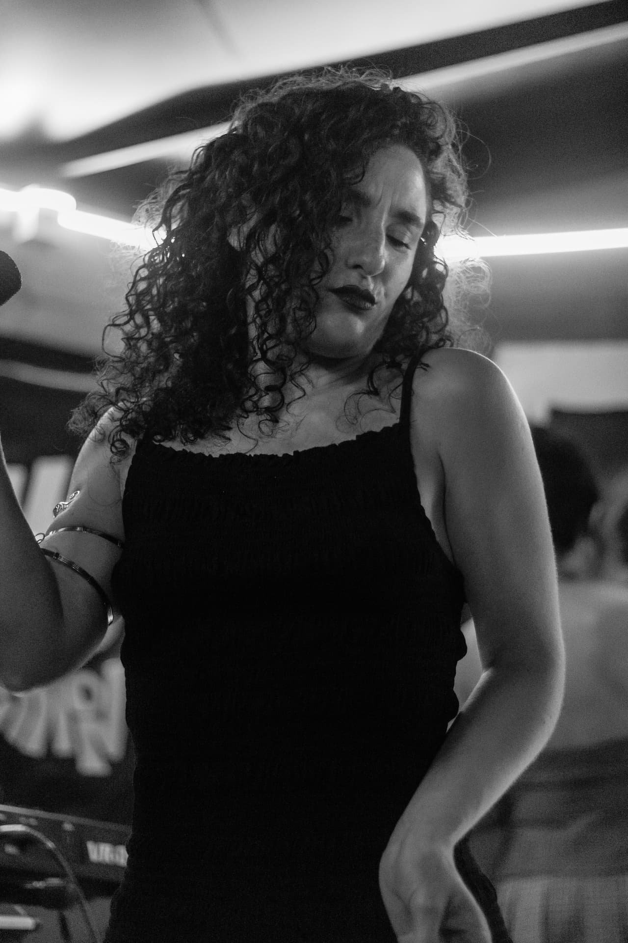 Em preto e branco, cantora de cabelos cacheados e vestido preto dança de olhos semicerrados